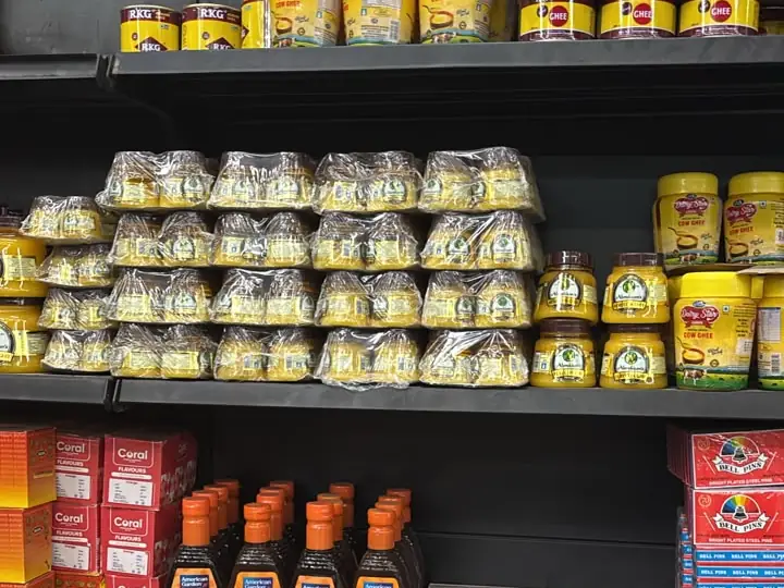Shelves of cow ghee jars and tins, with sauces and food colours below